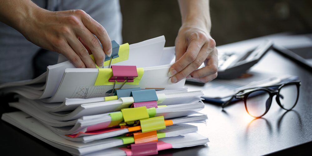 Manos ordenando una pila de documentos marcados con pestañas de colores